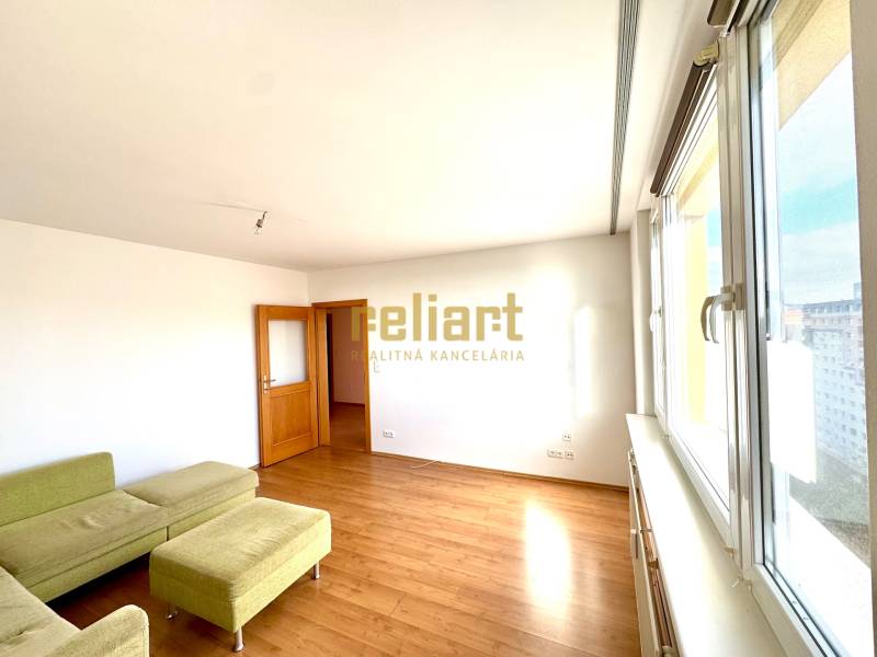 Zrekonštruovaný 3i byt na začiatku Petržalky, električka, les, výhľady - Obývacia izba s podlahou s dreveným dekorom, zelenou sedačkou a veľkými oknami v 3-izbovom byte.