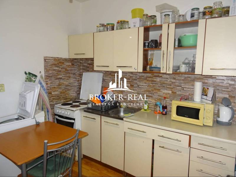 1 - izbový byt Košice, Popradská - Kuchyňa v 1-izbovom byte s kuchynskou linkou, spotrebičmi a dreveným dekorom podlahy.