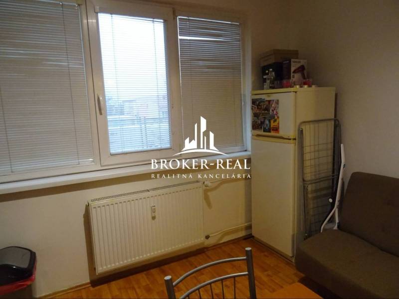 1 - izbový byt Košice, Popradská - Izba s oknom, prúžkovanými žalúziami, podlahou s dreveným dekorom a chladničkou v 1-izbovom byte.