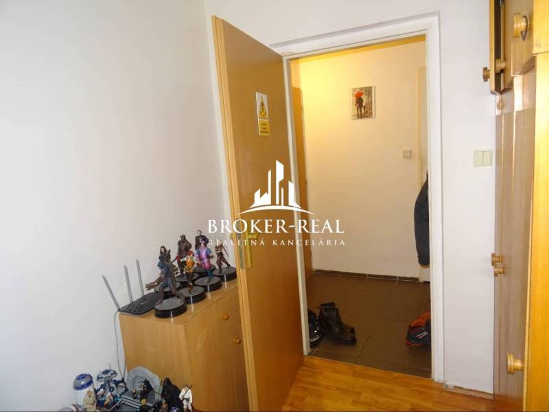 1 - izbový byt Košice, Popradská - Interiér 1-izbového bytu s figúrkami na skrinke a podlahou s dreveným dekorom.