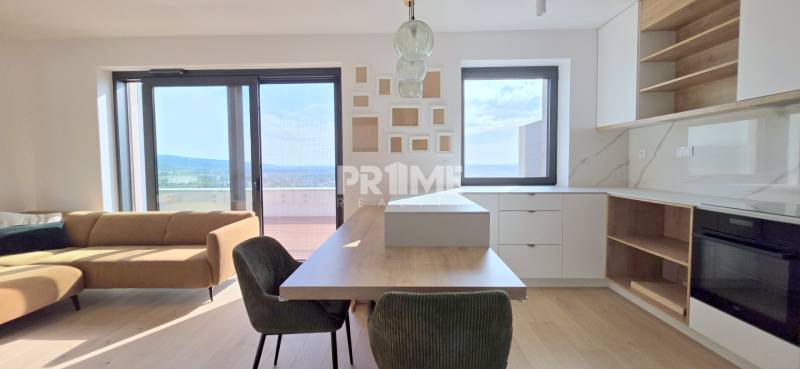 LUXUSNÝ 3i byt,PARKING,CHLADENIE,TERASA,Grand Koliba, Frankovská ulica - Svetlá obývacia izba s kuchyňou v 3-izbovom byte s veľkými oknami a hnedou sedačkou.