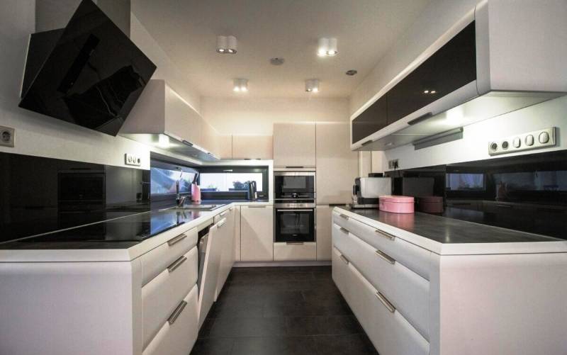 Priestranný 5-izbový rodinný dom s pohodlným dojazdom do Bratislavy  - Kuchyňa v rodinnom dome s čiernymi spotrebičmi, bielymi skrinkami a tmavou dlažbou.