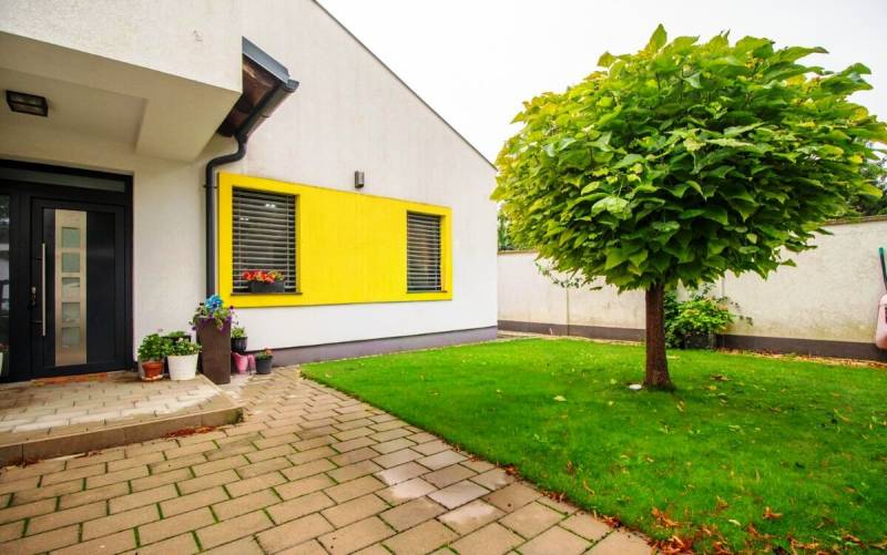 Priestranný 5-izbový rodinný dom s pohodlným dojazdom do Bratislavy  - Rodinný dom so žltým obkladom, dlažbou a zeleným trávnikom v Nitre.