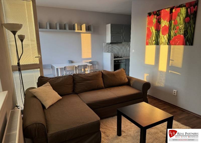 Prenájom 2-izb byt v uzavretom areáli Bratislava II - Obývacia izba s hnedou sedačkou, stolíkom a podlahou s dreveným dekorom v 2-izbovom byte.