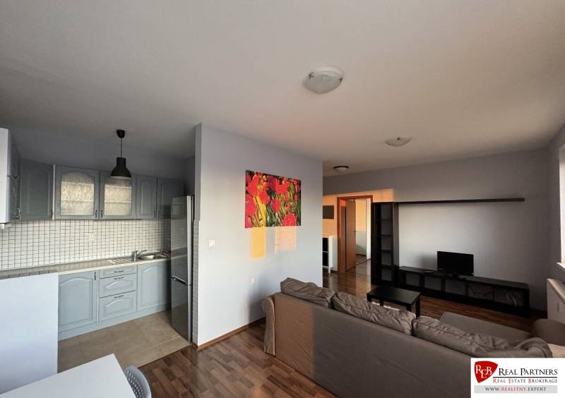 Prenájom 2-izb byt v uzavretom areáli Bratislava II - Obývacia izba s kuchyňou v 2-izbovom byte. Sedačka, televízia, kuchynská linka, podlaha s dreveným dekorom.