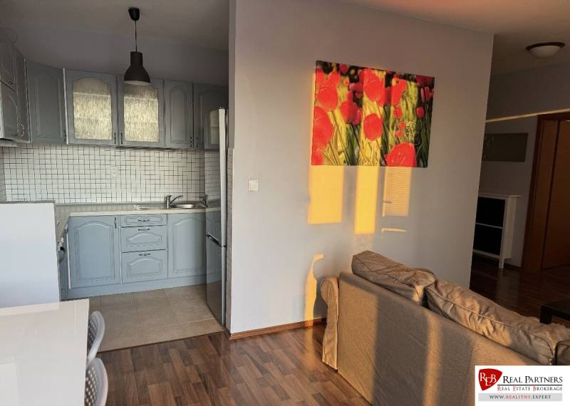 Prenájom 2-izb byt v uzavretom areáli Bratislava II - Kuchyňa s modrou linkou, stolom, pohovkou a podlahou s dreveným dekorom v 2-izbovom byte.