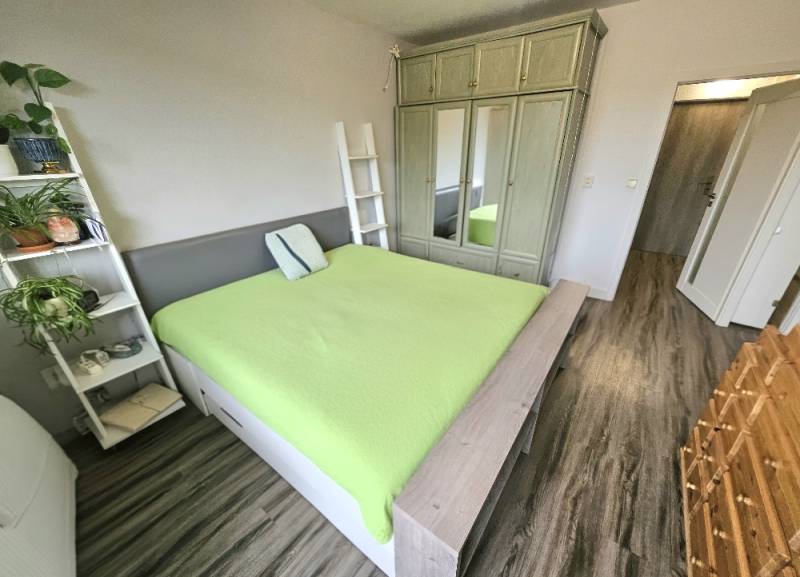 3 izbový byt Bánovce nad Bebravou 67 m2 / 3x BALKÓN / PIVNICA / - Spálňa v 3-izbovom byte s podlahou s dreveným dekorom a zelenou posteľou.