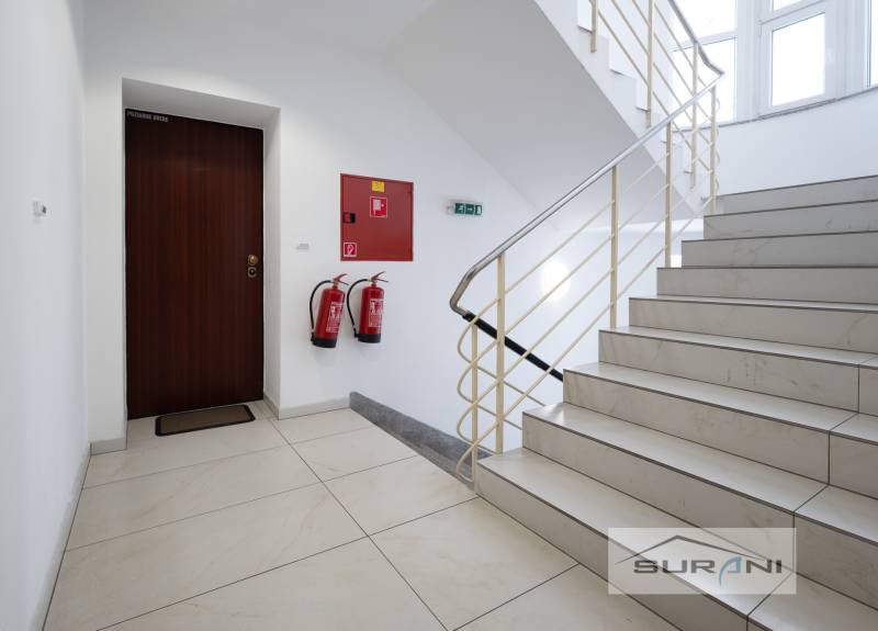  	 Bez Provízie | Kancelária 17m2 | Paulínyho ulica | Bratislava - Kancelárie s bielymi stenami, schodiskom a protipožiarnymi dverami, podlaha s dreveným dekorom.