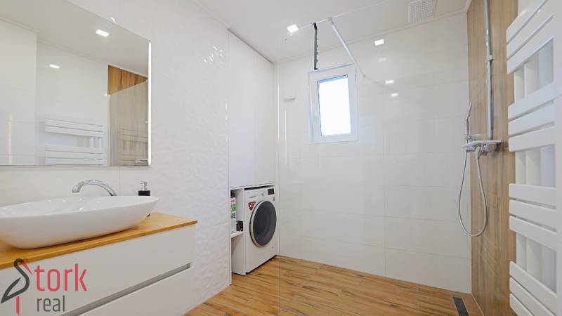 TOP - Rodinný dom s veľkým pozemkom - Dolný Hričov - Kúpeľňa s práčkou, sprchovým kútom, umývadlom a podlahou s dreveným dekorom v rodinnom dome.