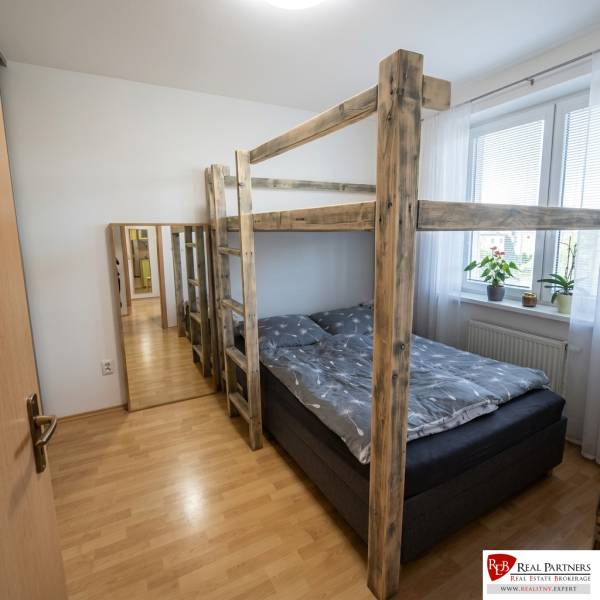 Na prenájom pekný 2-izbový byt s loggiou, Most pri BA - Spálňa v 2-izbovom byte s poschodovou posteľou, podlaha s dreveným dekorom a zrkadlo.