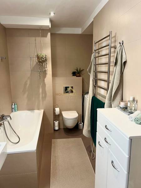 Prenájom 2,5 izbový byt, Trenčianska ulica, Bratislava II. Ružinov - Kúpeľňa v 2-izbovom byte s vaňou, zelenými rastlinami a úložnými skrinkami.