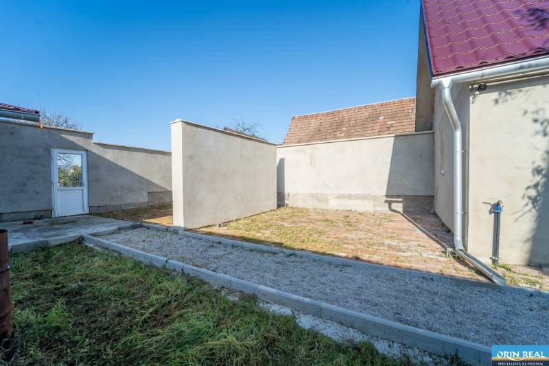 RD PO REKONŠTRUKCII spolu so STAVEBNÝM POZEMKOM na druhý dom - takmer  - Dvor rodinného domu na Kupeckého ulici v Pezinku s bránou a trávnatou plochou.