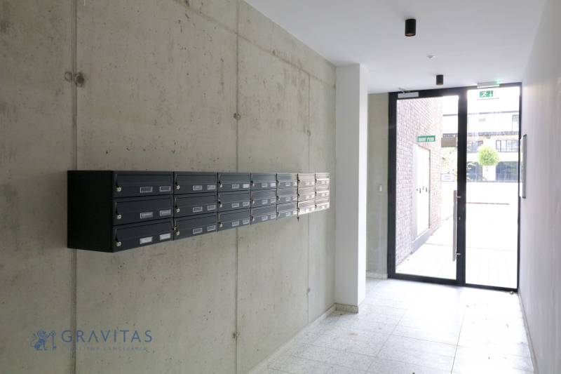 Komfortne vybavený 2-izbový byt v projekte 2 Sýpky - Poštové schránky na chodbe bytového domu s betónovými stenami a presklenými dverami.