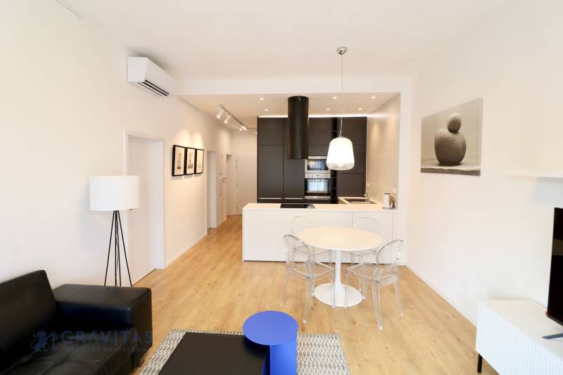 Komfortne vybavený 2-izbový byt v projekte 2 Sýpky - Obývacia izba s podlahou s dreveným dekorom, kuchynskou linkou a jedálenským stolom v 2-izbovom byte.