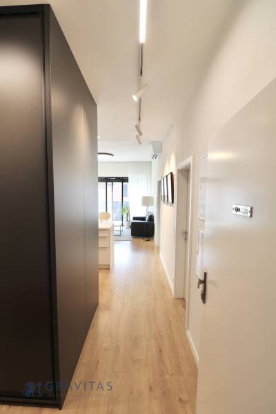 Komfortne vybavený 2-izbový byt v projekte 2 Sýpky - Chodba v 2-izbovom byte s podlahou s dreveným dekorom a moderným osvetlením.