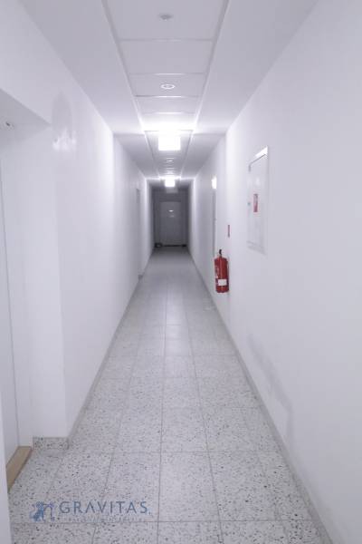 Komfortne vybavený 2-izbový byt v projekte 2 Sýpky - Tá úzka chodba s bielymi stenami, dlažbou a hasiacim prístrojom na stene.