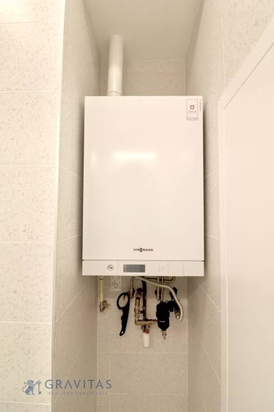 Komfortne vybavený 2-izbový byt v projekte 2 Sýpky - Biely kotol namontovaný na stene v 2-izbovom byte, s dlažbou okolo.