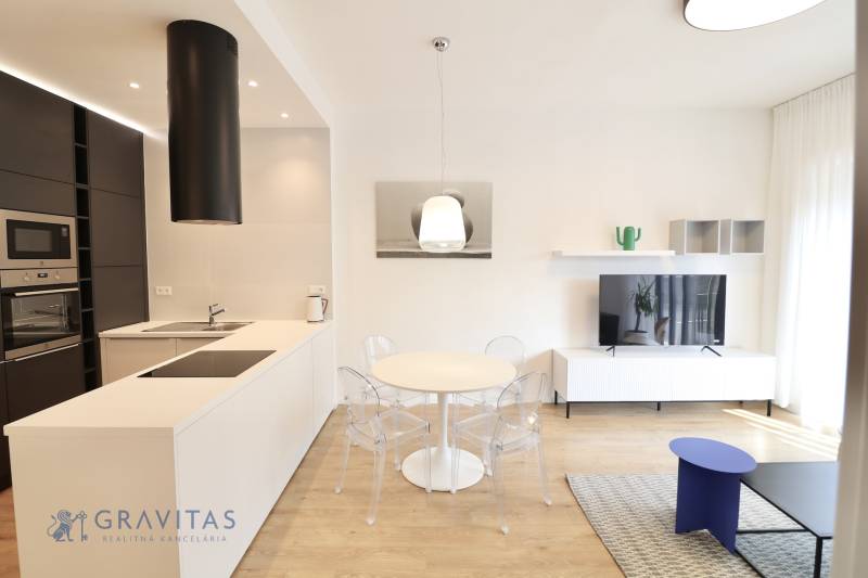 Komfortne vybavený 2-izbový byt v projekte 2 Sýpky - Obývacia izba v 2-izbovom byte s kuchyňou, jedálenským stolom a podlahou s dreveným dekorom.