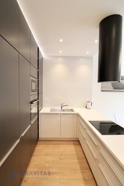 Komfortne vybavený 2-izbový byt v projekte 2 Sýpky - Kuchyňa s tmavými skriňami, bielou linkou a podlahou s dreveným dekorom v 2-izbovom byte.