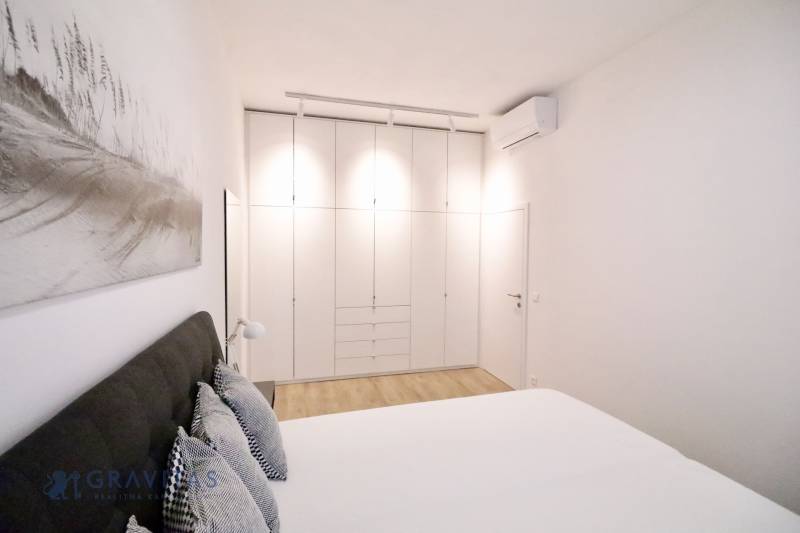 Komfortne vybavený 2-izbový byt v projekte 2 Sýpky - Svetlá spálňa s bielou vstavanou skriňou a podlahou s dreveným dekorom v 2-izbovom byte.