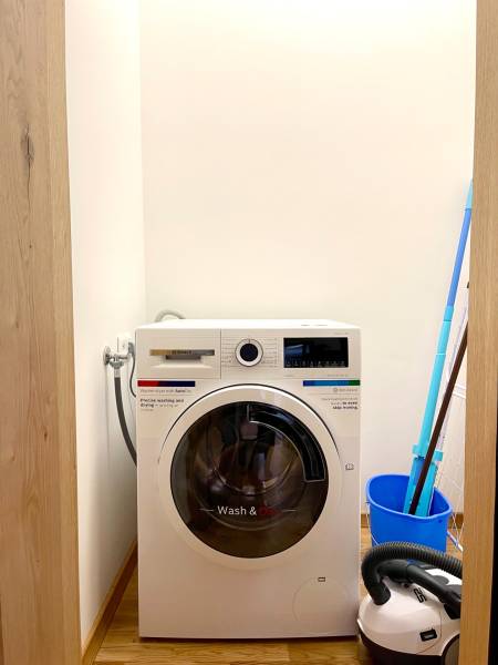 I 3 i byt s parkovaním v rezidenčnom komplexe METROPOLIS - Práčka so sušičkou v 3-izbovom byte, podlaha s dreveným dekorom, vedľa vedro a vysávač.