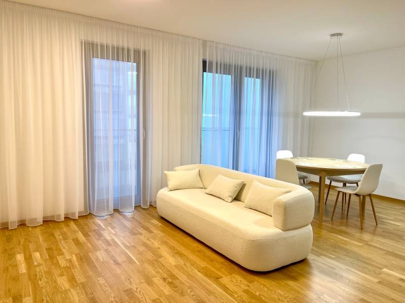 I 3 i byt s parkovaním v rezidenčnom komplexe METROPOLIS - Obývacia izba s béžovou pohovkou, okrúhlym stolom a podlahou s dreveným dekorom.