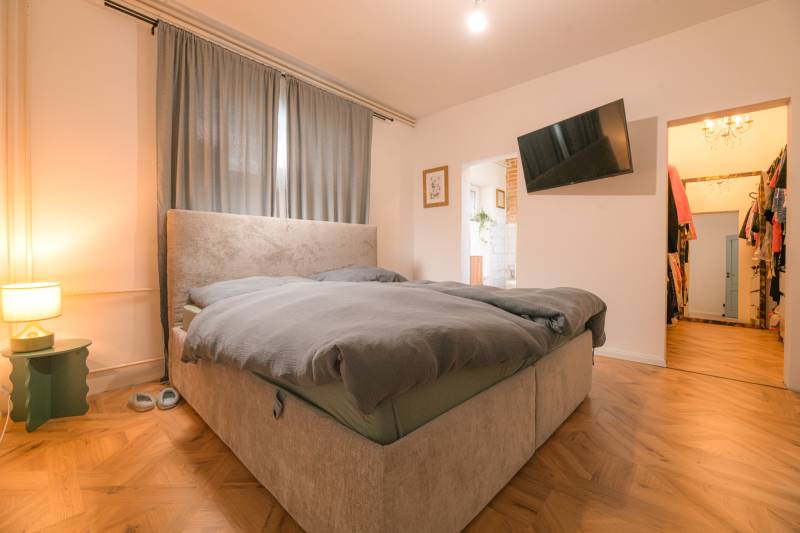 Na predaj zrekonštruovaný dom na Štefánikovej ulici, Trenčín - Spálňa v rodinnom dome s posteľou, závesmi, TV a podlahou s dreveným dekorom.