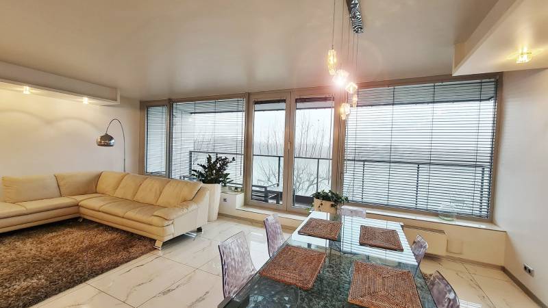 River Park / Luxusný 3-izb. byt s famóznym výhľadom na Dunaj, terasy - Obývacia izba 3-izbového bytu s veľkými oknami, krémovou sedačkou a jedálenským stolom.