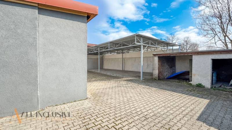 PRAKTICKÉ SKLADOVÉ PRIESTORY  | DOPRAVNÁ | TOPOĽČANY - Nádvorie na ulici Dopravná s prístreškom, sklady a haly, jasná obloha, stromy bez listov.