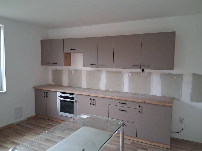 PREDAJ – 4-izbový rodinný dom v radovej zástavbe s garážou - Kuchyňa v rodinnom dome s podlahou s dreveným dekorom a šedými skrinkami.