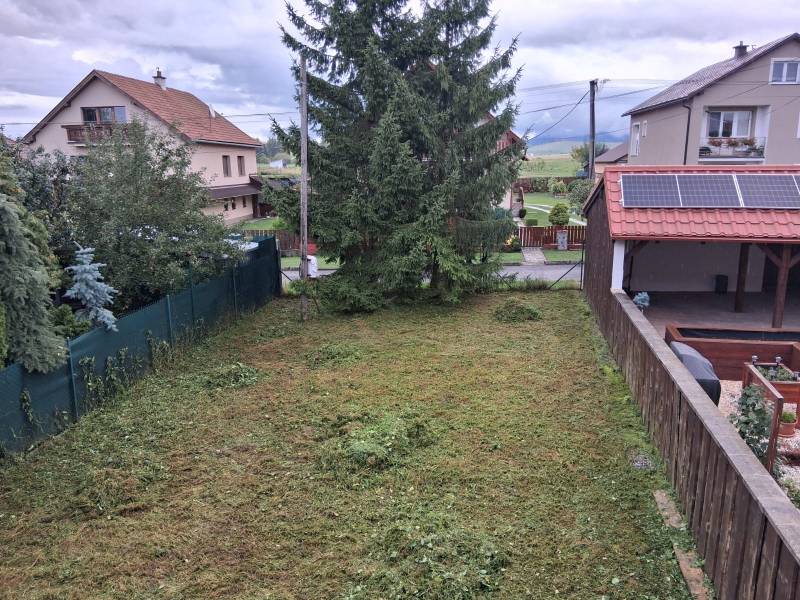 PREDAJ – 4-izbový rodinný dom v radovej zástavbe s garážou - Záhrada pri rodinnom dome v Ľubeli s udržiavaným trávnikom a hustými stromami.