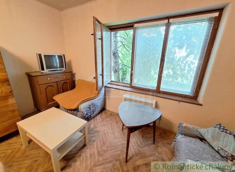 Pôvodný domček v obci Nová Vieska - Obývacia izba s TV, veľkým oknom a podlahou s dreveným dekorom v rodinnom dome.