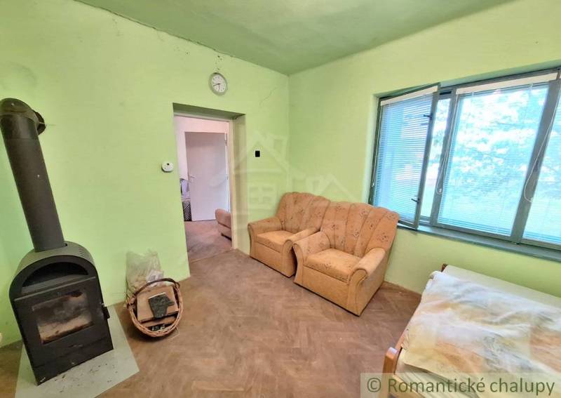 Pôvodný domček v obci Nová Vieska - Izba v rodinnom dome s kachľami, dvoma kreslami a podlahou s dreveným dekorom.