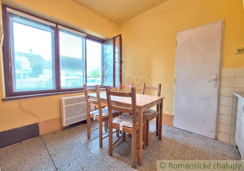 Pôvodný domček v obci Nová Vieska - Jedáleň v rodinnom dome s jednoduchým dreveným stolom a stoličkami, žlté steny.