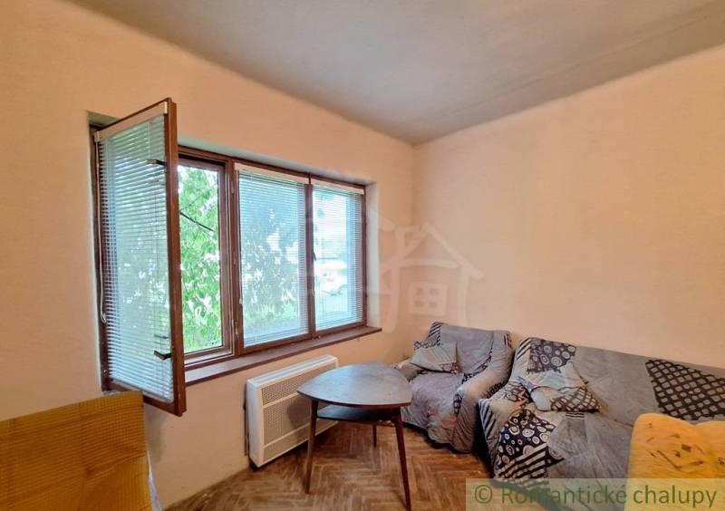 Pôvodný domček v obci Nová Vieska - Obývacia izba v rodinnom dome s pohovkou, stolíkom a oknami, podlaha s dreveným dekorom.