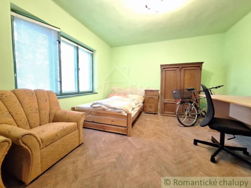 Pôvodný domček v obci Nová Vieska - Izba so zelenými stenami obsahuje posteľ, pohovku, skriňu a bicykel na podlahe s dreveným dekorom.