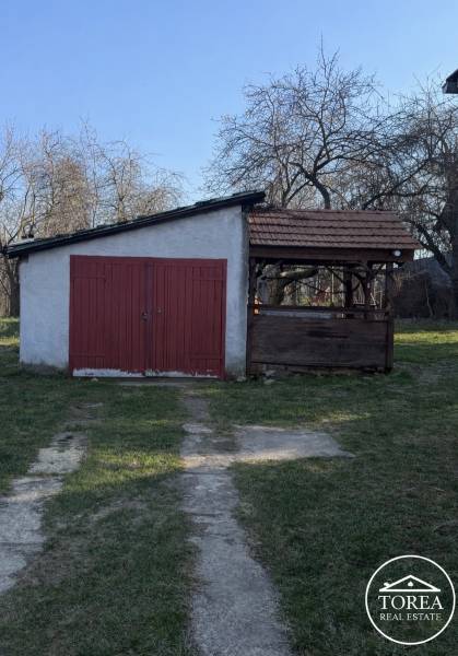 Rodinný dom s pozemkom 1978 m2  v  lokalite – Prašice. - Rodinný dom v Prašiciach s prístreškom a veľkými červenými dverami na záhrade.