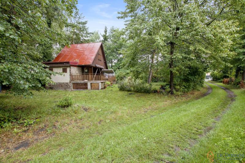 NA PREDAJ CHATA V REKREAČNEJ OBLASTI RUDAVA, OBEC MALÉ LEVÁRE - Chata v Malých Levároch obklopená zeleňou s červenou plechovou strechou a trávnatou cestou.