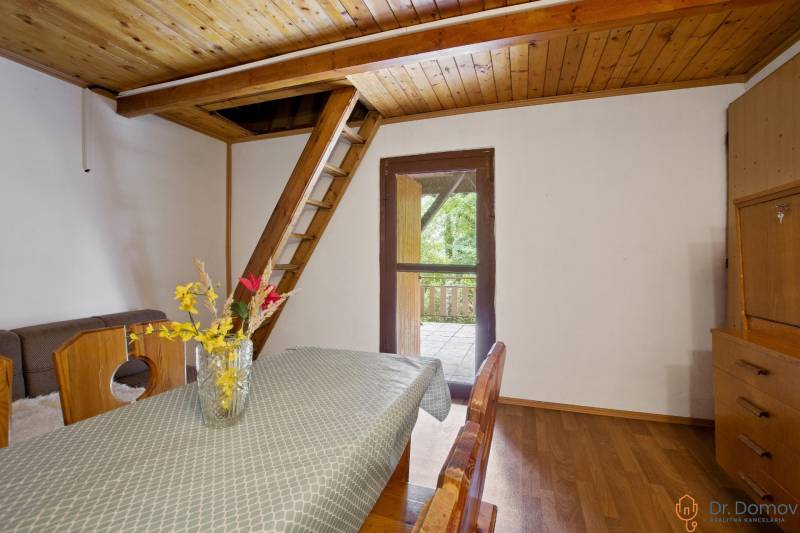 NA PREDAJ CHATA V REKREAČNEJ OBLASTI RUDAVA, OBEC MALÉ LEVÁRE - Jedálenský stôl s kvetmi, schody na poschodie, podlaha s dreveným dekorom.