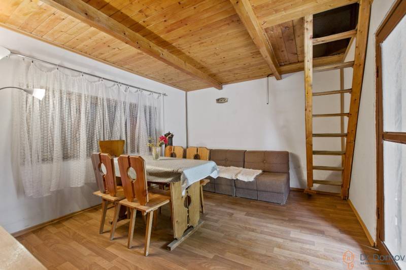 NA PREDAJ CHATA V REKREAČNEJ OBLASTI RUDAVA, OBEC MALÉ LEVÁRE - Interiér chaty s dreveným schodiskom, jedálenským stolom a podlahou s dreveným dekorom.