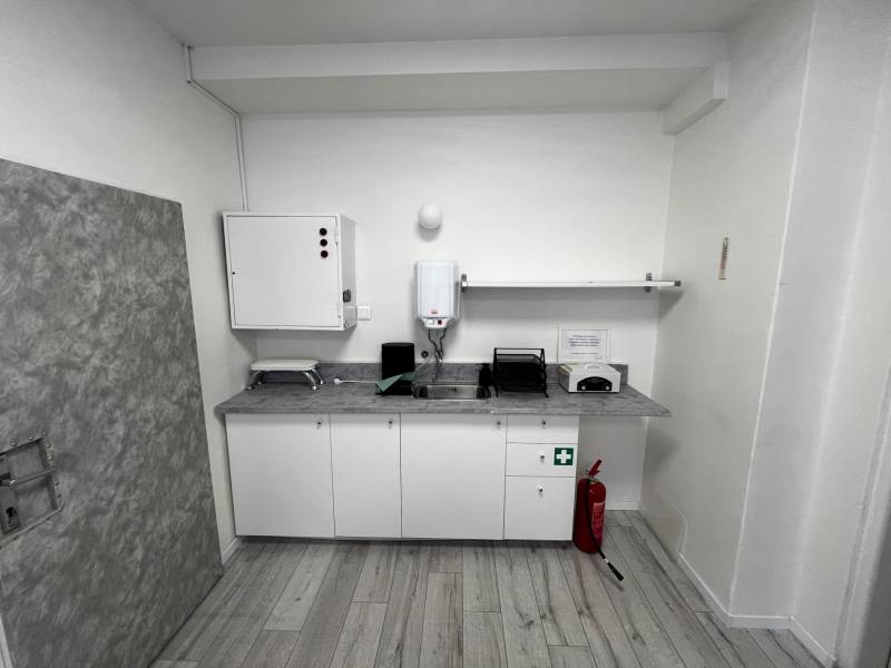 Prenájom ordinácie v zdravotnom stredisku Saratovská 24, Bratislava. - Interiér obchodných priestorov s kuchynským kútom, umývadlom a protipožiarnym vybavením na podlahe s dreveným dekorom.