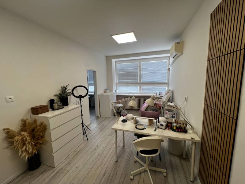 Prenájom ordinácie v zdravotnom stredisku Saratovská 24, Bratislava. - Biela miestnosť s pracovným stolom, lampami a dekoráciou na podlahe s dreveným dekorom.