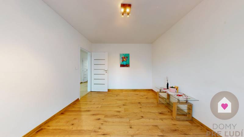 MALÉ LEVÁRE-Predaj  3i modernej novostavby RD s tep. čerpadlom + garáž - Izba v rodinnom dome s podlahou s dreveným dekorom a dekoračným obrazom na stene.