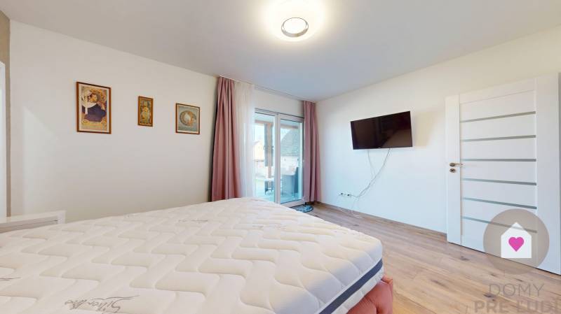 MALÉ LEVÁRE-Predaj  3i modernej novostavby RD s tep. čerpadlom + garáž - Spálňa v rodinnom dome s podlahou s dreveným dekorom a televízorom na stene.