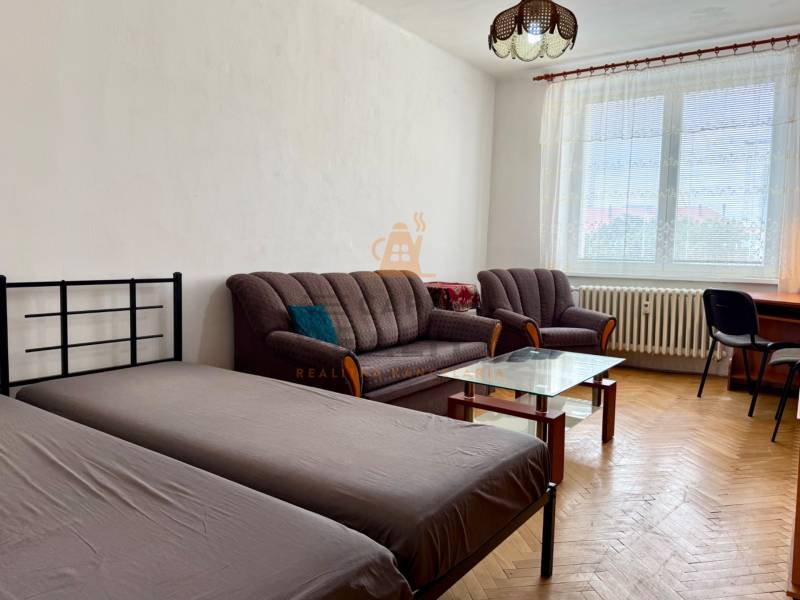 PRENÁJOM 1 izbový byt, 40 M2, Bratislava, Ružinov, Košická ulica, NIVY - Izba s podlahou s dreveným dekorom, posteľou, gaučom, stolíkom a písacím stolom.