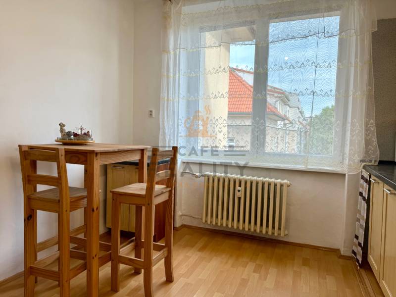 PRENÁJOM 1 izbový byt, 40 M2, Bratislava, Ružinov, Košická ulica, NIVY - Jedálenský kút so stolom z dreva, podlaha s dreveným dekorom, záclona na okne.