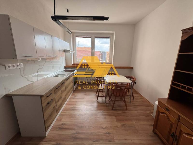 Prenajmem 1 izbový byt v Nových Zámkoch - Kuchyňa v 1-izbovom byte so stolom, stoličkami a podlahou s dreveným dekorom.