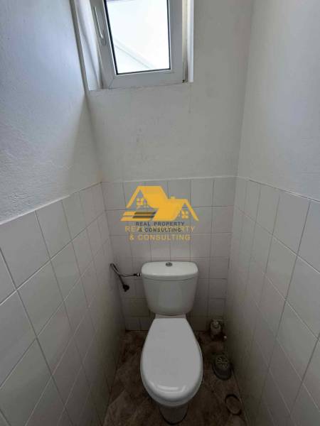 Prenajmem garsónku v Nesvadoch - Kompaktná toaleta s oknom, biele dlaždice, podlaha s dreveným dekorom.