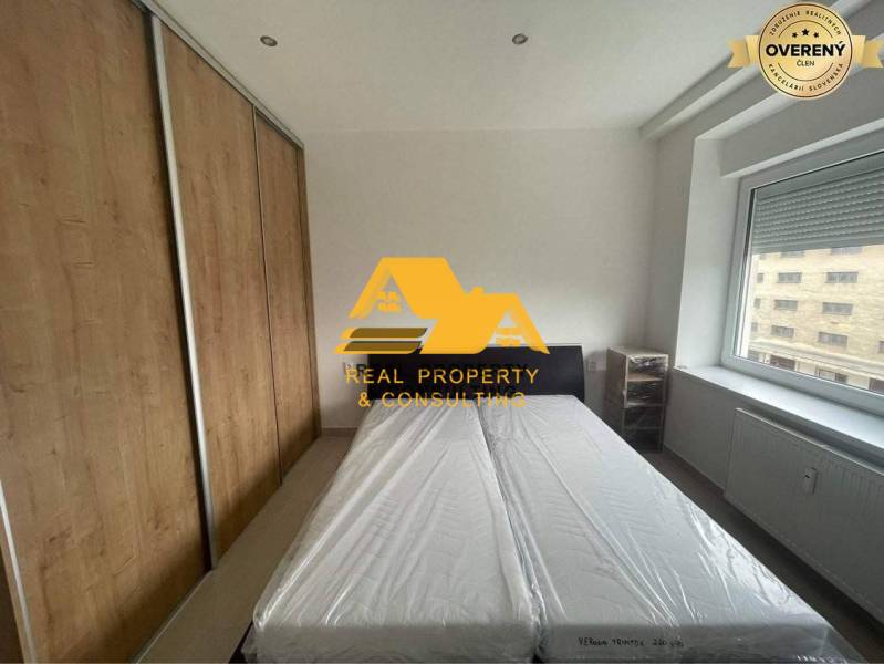 Prenajmem zariadený 3 izbový byt v Nových Zámkoch - Spálňa v 3-izbovom byte s posteľou, vstavanou skriňou a oknom s výhľadom.