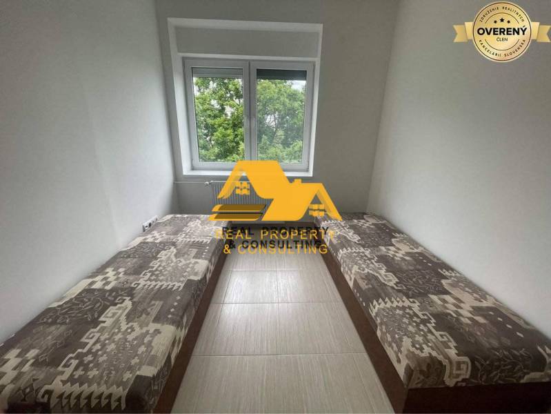 Prenajmem zariadený 3 izbový byt v Nových Zámkoch - Útulná izba v 3-izbovom byte s dvoma postelemi a výhľadom na zeleň.